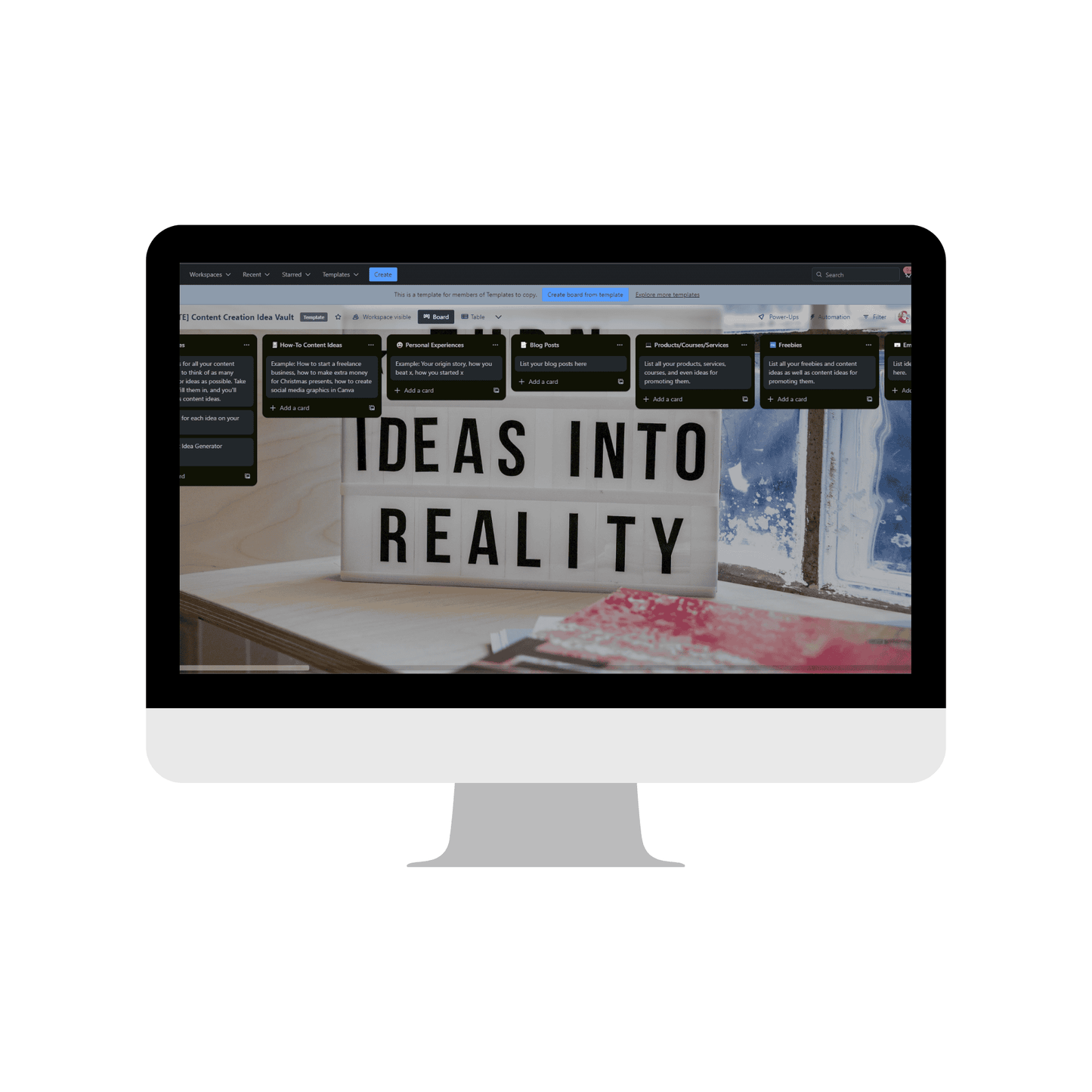 A monitor showcases the Content Catalyst SEO Hub by ContentPreneur Biz Shop, featuring a digital planning board with various cards. In the foreground, a lightbox on a wooden surface displays "IDEAS INTO REALITY," perfectly placed near a window that provides an inspiring view of the outdoors, ideal for stimulating new ideas for content creation.